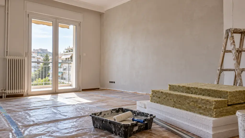 Empty apartment being renovated, with protected flooring, painting tools and insulation samples