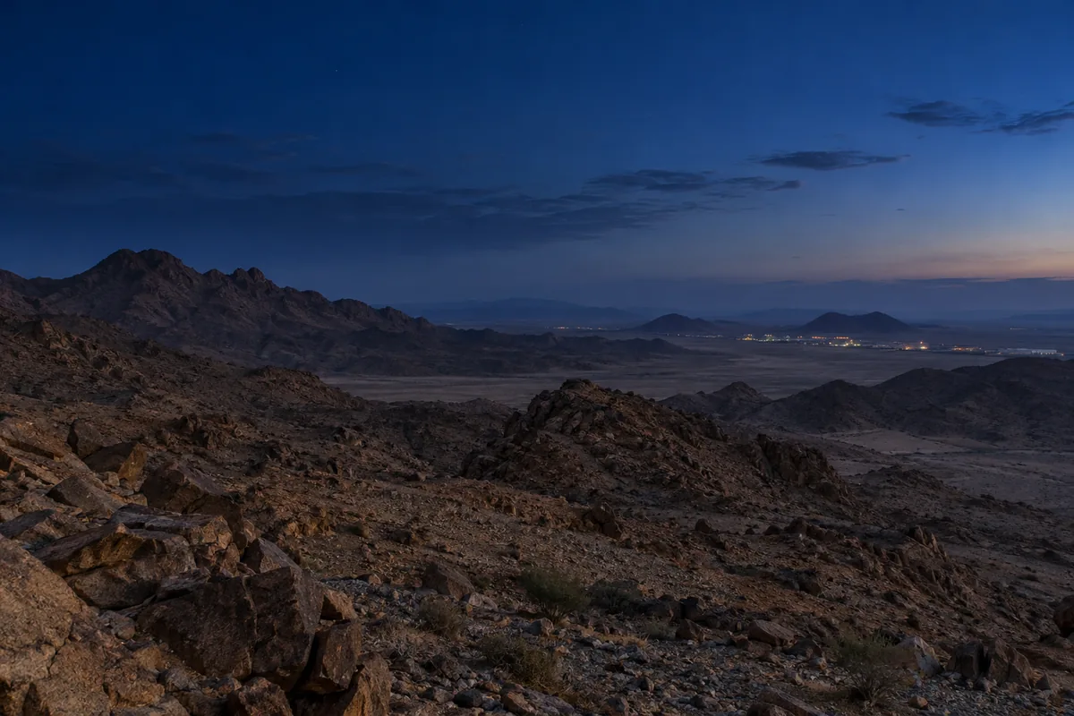 Rocky mountain landscape with distant settlement lights before dawn