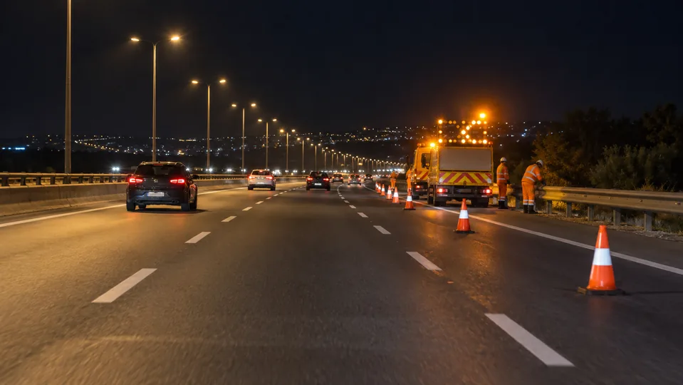 Traffic cones and a maintenance vehicle on a road shoulder at night